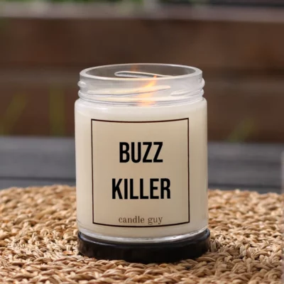 Burning anti-mosquito candle with the quote “Buzz Killer” in a white jar in a cozy setting